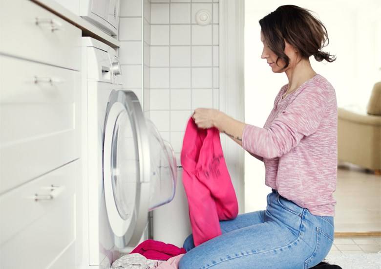 Mujer arrodillada dobla camisa de color rosa frente a lavadora