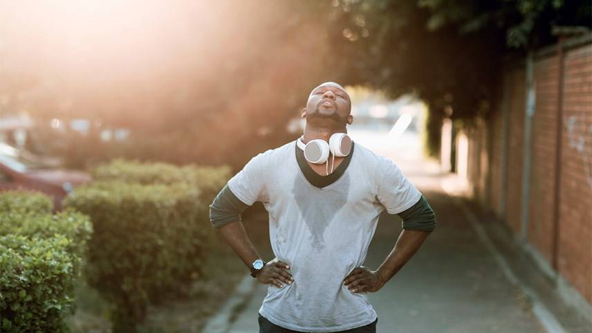 Hombre afroamericano con playera gris sudada con audífonos en cuello respira