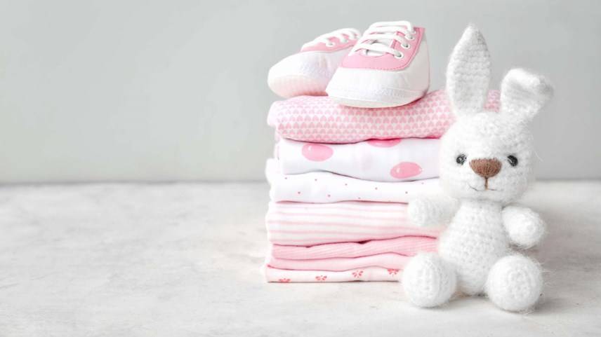 conejo de peluche blanco junto a ropa y zapatos de bebé