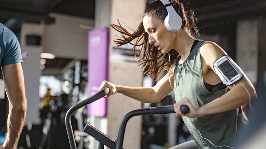 Mujer con audífonos y haciendo ejercicio en aparato de gimnasio
