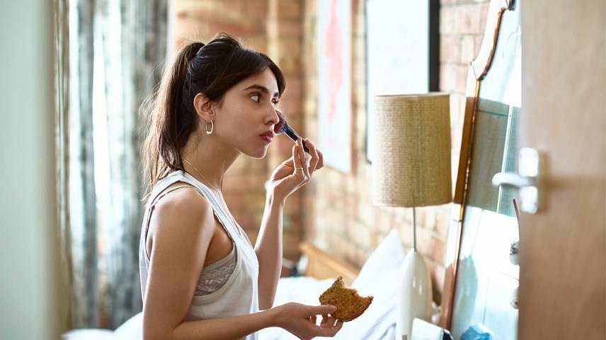 Mujer usa brocha para maquillarse frente a espejo en casa