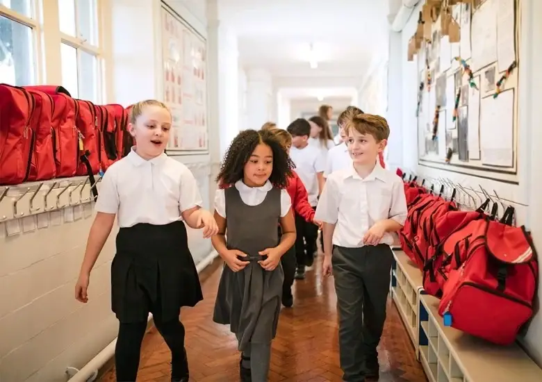 Niños en escuela caminan por pasillo vestidos con uniformes