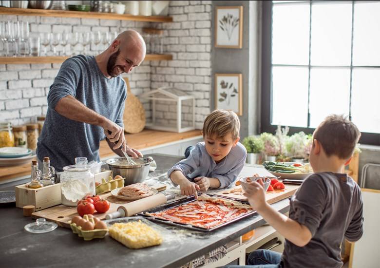 Hombre con playera azul prepara comida junto a dos niños en cocina